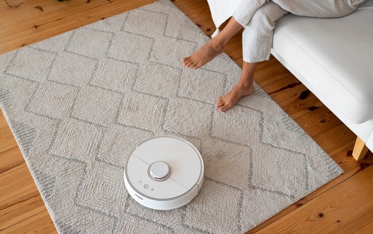 Una persona en el salón de su casa junto a un robot aspirador en marcha