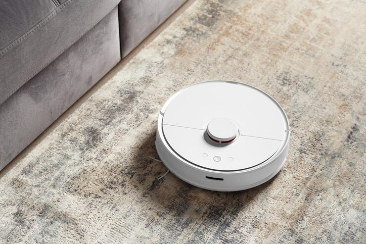 Robot aspirador blanco limpiando la alfombra de un salón junto al sofá
